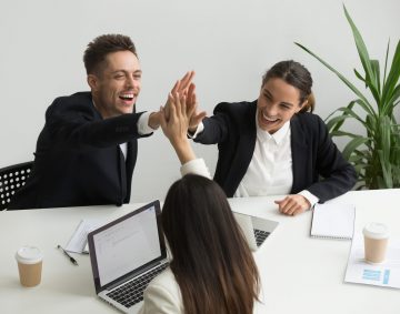 Excited millennial office team giving high five together, business people celebrating good teamwork result or common goal achievement, expressing unity, good corporate relations, teambuilding concept