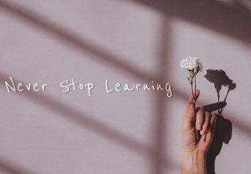 Never stop learning quote on a hand holding flower background