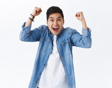 Waist-up portrait of happy, excited young smiling man shouting hooray or yes, raising hands up, fist pump in joy, rejoicing over win, achieve goal, celebrate victory or success, white background.